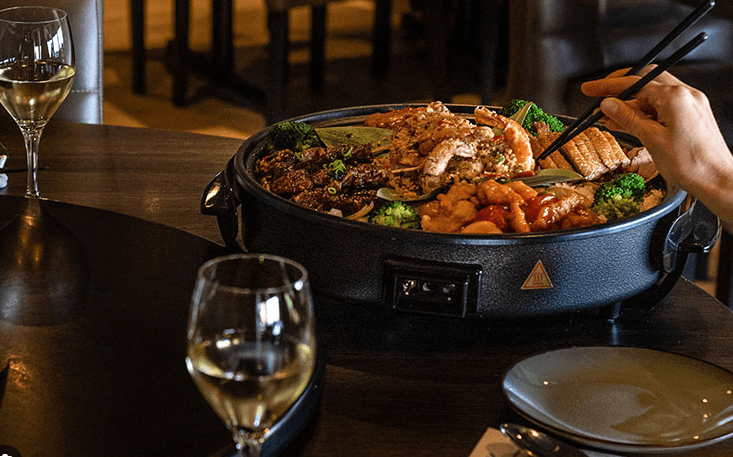 Restaurant: gedeelde schotel met Aziatische gerechten, geglazuurd vlees en gamba’s op een gedekte tafel in een restaurant.