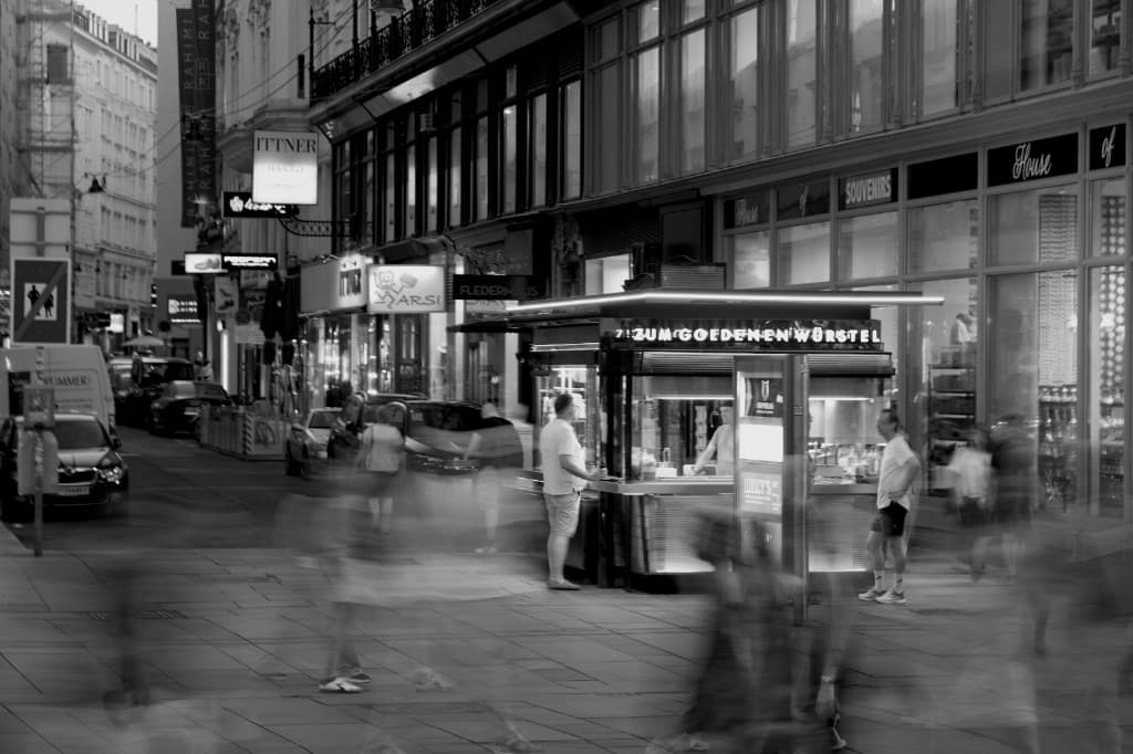 Verlichte toonbank en klanten op straat in de avond — typisch voor een nachtwinkel